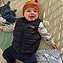 baby, blanket, child, clothing, cute, face, happy, hat, headwear, indoor, infant, lying_down, pacifier, patterned_blanket, puffer_vest, smiling, soft_toys, striped_socks, toys, warm