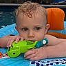 toddler, child, baby, pool, water, inflatable, toy, green_toy, blue, orange, curly_hair, wet_hair, outdoor, summer, play, float, face, hands, expression, evening