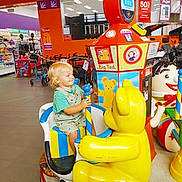 Ollie-Ray joined the competition — help win amazing prizes! child, toddler, kiddie_ride, toy_bear, amusement_ride, shopping_center, retail_store, stroller, colorful, smile, blonde_hair, seat, pole, play, indoor, mascot_face, signage, tiled_floor, aisle, portrait