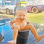 Riley is registered to the contest to win money with this photo: child, toddler, bucket, water, playing, smiling, barefoot, outdoor, sunlight, wet, laughing, concrete, hose, car, van, trash_bin, vehicle, playtime, happy, portrait