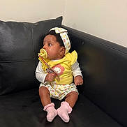 Vivian is registered to the contest to win money with this photo: baby, infant, pacifier, yellow_clothing, headband, sitting, couch, black_leather, pink_socks, indoor, cute, child, portrait, person, looking_sideways, wall, home, young_child, adorable, comfortable