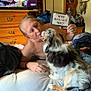 person, dog, bed, sign, text, indoor, furniture, television, wooden_drawer, blanket, casual, interaction, pet, rescue, home, comfort, relaxation, candid, love, companionship