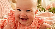 Callie Rae is registered to the contest to win money with this photo: baby, smiling, infant, portrait, close_up, cute, child, flower, soft_lighting, blanket, indoors, dress, happy, face, skin, cheeks, eyes, head, furniture, cozy