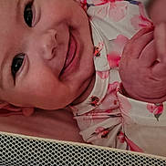 Callie Rae joined the competition — help win amazing prizes! baby, smiling, face, hand, floral_clothing, infant, closeup, cute, lying_down, mesh_barrier, pink, skin, cheeks, eyes, portrait, child, happy, indoors, newborn, soft_light