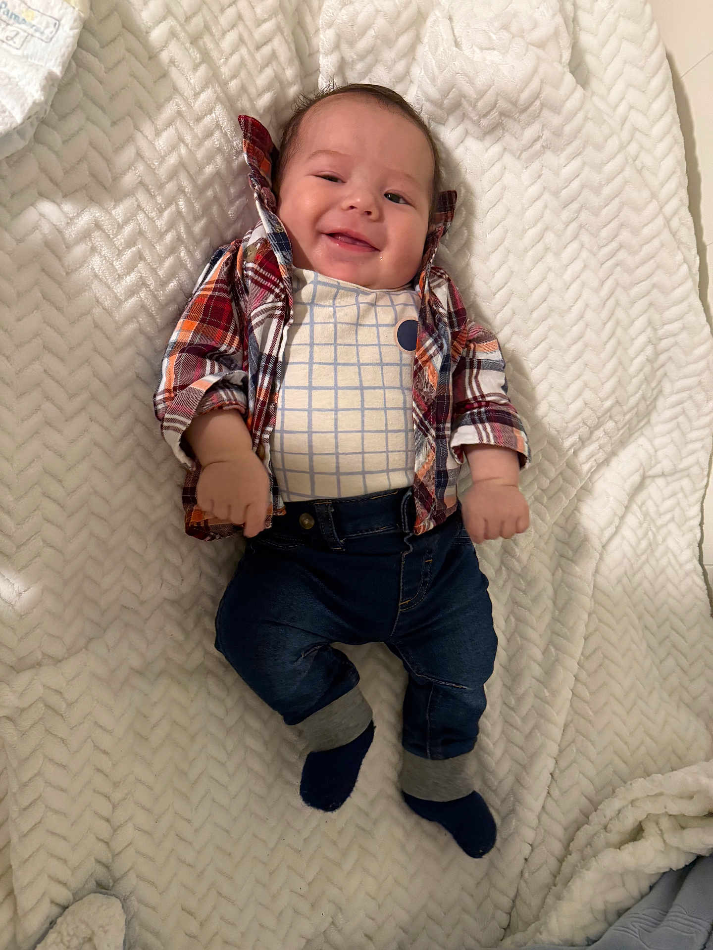 Ethan Mateo is registered to the contest to win money with this photo: baby, infant, smiling, plaid_shirt, jeans, socks, blanket, cozy, happy, lying_down, cute, child, fashion, clothing, portrait, indoor, soft_texture, face, hands, feet