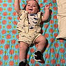 Ethan Mateo joined the competition — help win amazing prizes! baby, child, infant, quilt, patterned_blanket, clothing, fish_print, sneakers, pillow, happy, raised_arms, lying_down, cute, indoors, person, footwear, smiling, shorts, shirt, fabric