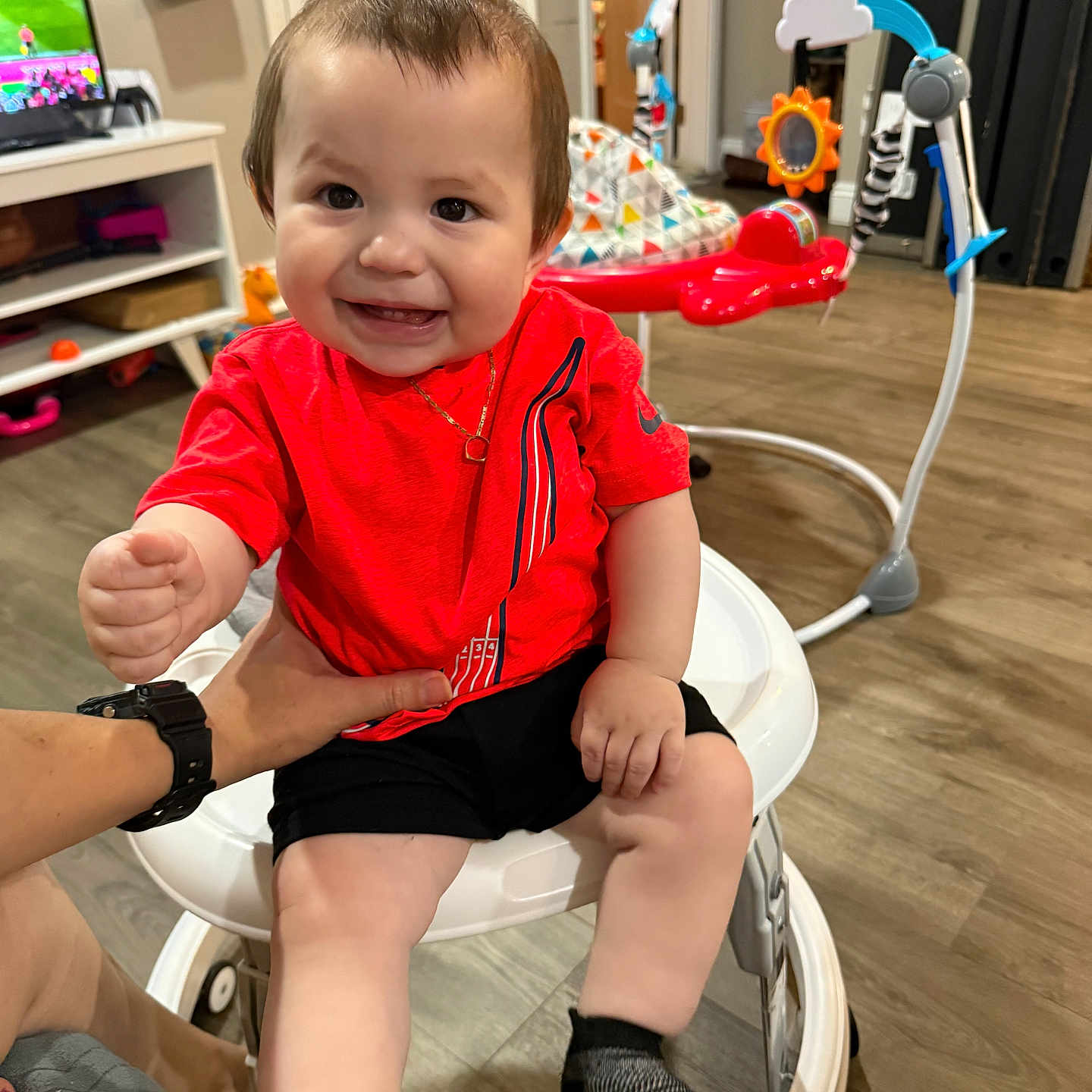 Ethan Mateo joined the competition — help win amazing prizes! baby, child, smile, red_shirt, walker, indoor, hand, toy, floor, person, furniture, television, activity_center, happy, clothing, shorts, socks, living_room, wood_floor, home