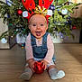 baby, blurred_background, celebration, child, christmas_tree, cute, denim_overalls, festive, floor, happy, holiday, indoor, ornament, pink_shirt, red_ball, reindeer_antlers, seasonal, smiling, socks, winter