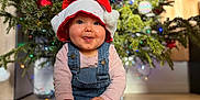 Capucine a rejoint le concours — aidez-le/la à gagner de superbes lots ! baby, celebration, child, christmas, christmas_tree, cute, decorations, festive, festivity, happy, holiday, indoor, ornament, overalls, portrait, santa_hat, seasonal, smiling, sock, wooden_floor