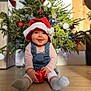 baby, celebration, child, christmas, christmas_tree, cute, decorations, festive, festivity, happy, holiday, indoor, ornament, overalls, portrait, santa_hat, seasonal, smiling, sock, wooden_floor