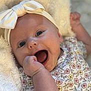 Lily is registered to the contest to win money with this photo: baby, infant, smiling, headband, bow, floral_dress, hand, face, blue_eyes, skin, blanket, soft_texture, cute, happy, portrait, closeup, child, newborn, expression, lying_down