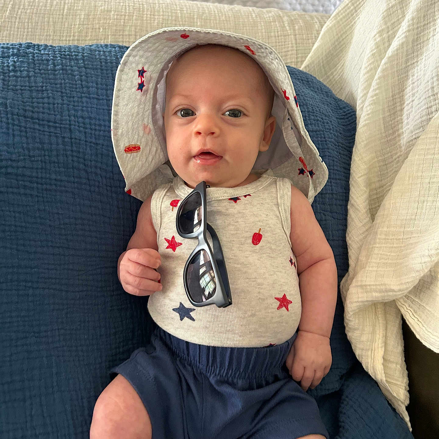 Rj joined the competition — help win amazing prizes! baby, clothing, comfort, cushion, cute, face, footwear, hat, headwear, indoor, infant, person, quilt, relaxing, seated, shorts, skin, smile, sunglasses, tank_top