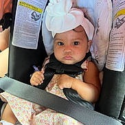 Jasmari joined the competition — help win amazing prizes! baby, infant, child, car_seat, safety_harness, seatbelt, bow_headband, floral_dress, toy, sitting, portrait, face, eyes, serious_expression, vehicle, automobile, interior, travel, warning_label,  안전