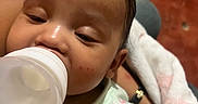 Jasmari joined the competition — help win amazing prizes! baby, infant, bottle, feeding, sleepy, face, portrait, close_up, blanket, wrapped, onesie, clothing, sitting, indoor, cozy, brown_hair, head, eyes, nursery, caregiving