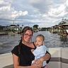 Tru is registered to the contest to win money with this photo: woman, baby, boat, water, canal, dock, sky, clouds, glasses, braid, smile, outdoor, nature, vacation, summer, family, holding, casual_clothing, relaxation, travel