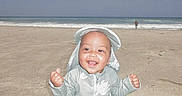 Tru is registered to the contest to win money with this photo: baby, barefoot, beach, child, clothing, happy, nature, ocean, outdoor, person, sand, sitting, sky, smiling, summer, sunhat, sunny, vacation, water, waves