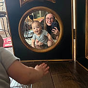 Tru is registered to the contest to win money with this photo: baby, carpet, casual_clothing, child, crawling, furniture, glasses, hand, happy, home, indoor, living_room, mirror, person, phone, portrait, reflection, smiling, woman, wooden_floor