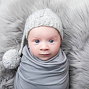 Léandro a rejoint le concours — aidez-le/la à gagner de superbes lots ! baby, infant, knitted_hat, pom_pom, gray_wrap, fur_background, blue_eyes, portrait, cute, newborn, soft_texture, cozy, close_up, child, face, smile, warm_clothing, studio_photo, headwear, lying_down