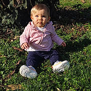 Chelsea participe au concours pour gagner de l'argent avec cette photo : baby, toddler, child, sitting, outdoor, grass, greenery, sunlight, pink_jacket, hoodie, sneakers, shoes, blue_eyes, leaves, park, portrait, curious_expression, ground, shadow, casual_clothing