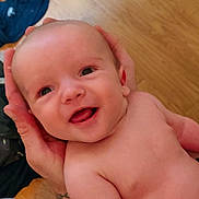Jax is registered to the contest to win money with this photo: baby, smiling, happy, face, head, hands, skin, child, infant, portrait, bare_chest, person, cute, newborn, indoor, floor, wooden_floor, closeup, expression, joy