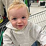 toddler, child, shopping_cart, supermarket, hoodie, jeans, blonde_hair, blue_eyes, person, grocery, indoor, smiling, curious, clothing, retail, store_shelves, casual, shopping, young_child, portrait