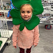 Angel is registered to the contest to win money with this photo: child, girl, face, green_shamrock_mask, costume, store, aisle, shelf, snacks, clothing, pink_sweater, maroon_pants, shoes, floor, shopping_cart, smile, portrait, indoor, retail, holiday