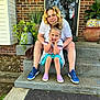 child, woman, smiling, steps, porch, brick_wall, plants, potted_plant, door, curly_hair, casual_clothing, sneakers, purple_shoes, blue_shoes, outdoor, daylight, happy, family, together, portrait