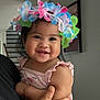 Gabriela is registered to the contest to win money with this photo: baby, child, smiling, flower_crown, cute, indoor, person, happy, portrait, holding, hand, pink_clothing, flamingo_pattern, toddler, face, dark_hair, skin, infant, closeup, family