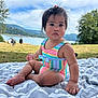 Gabriela joined the competition — help win amazing prizes! toddler, child, baby, swimsuit, striped_clothing, outdoor, lake, mountains, trees, blanket, grass, summer, nature, portrait, sitting, person, cute, young_child, daylight, scenic