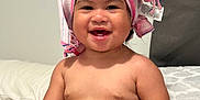 Gabriela is registered to the contest to win money with this photo: baby, child, smiling, towel, pink_pants, bed, blanket, indoor, cute, happy, skin, person, infant, headwear, funny, portrait, sitting, playful, young, comfort
