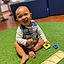 Malachi is registered to the contest to win money with this photo: toddler, child, smiling, playing, toy, shape_blocks, indoor, carpet, green, happy, sitting, baby, clothing, plaid, foot, furniture, blurred_background, person, room, cute