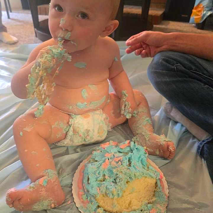 Persephoneia is registered to the contest to win money with this photo: adult_hand, baby, birthday, cake, celebration, child, cute, diaper, face, feet, food, frosting, fun, hands, indoor, messy, plastic_sheet, playful, sitting, smiling