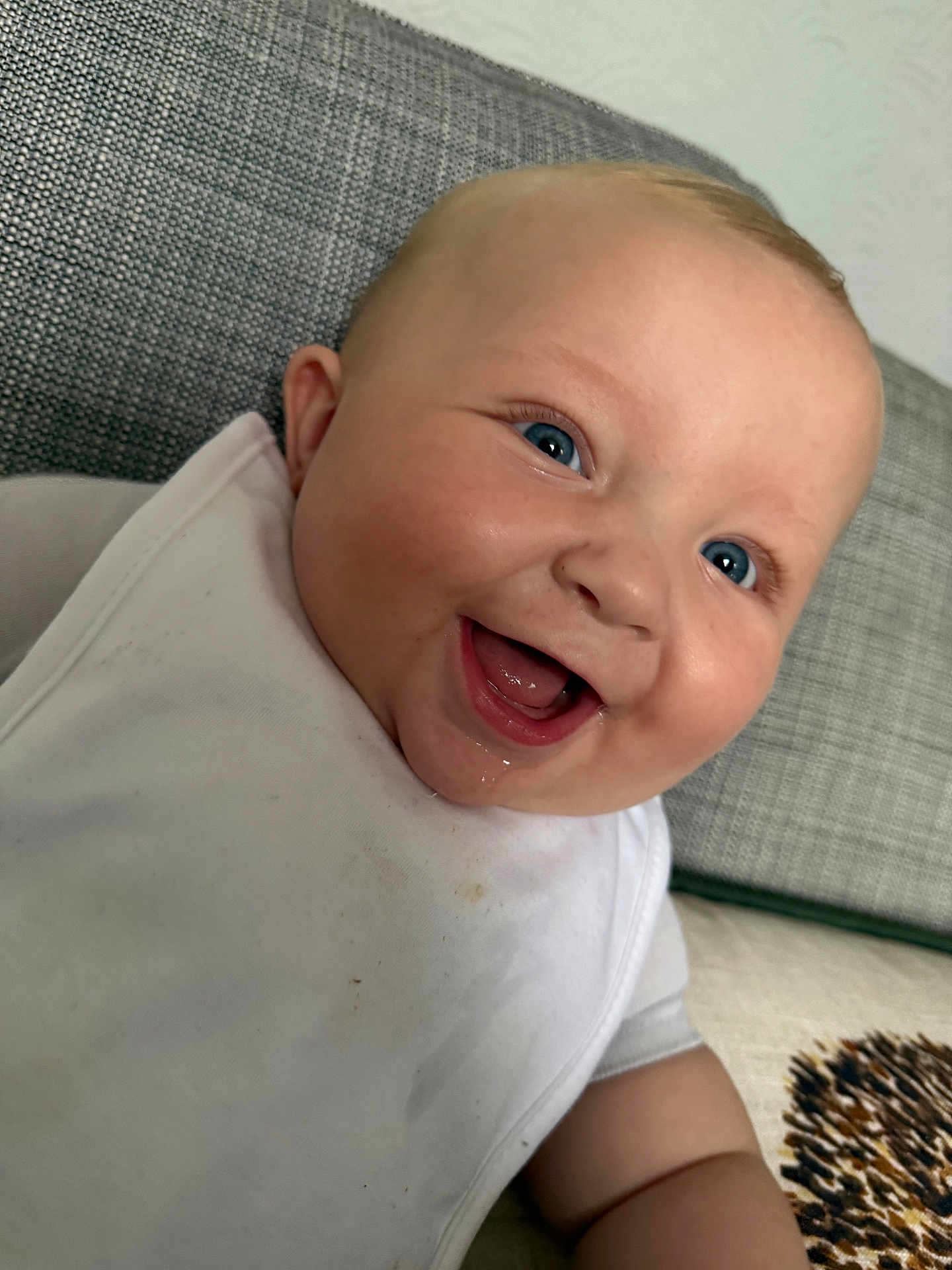 Colby-Reece is registered to the contest to win money with this photo: arm, baby, bib, blue_eyes, child, close_up, couch, cute, drool, fabric, face, happy, indoor, infant, person, portrait, skin, smile, texture, young