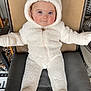 Ivy is registered to the contest to win money with this photo: baby, child, onesie, white, fuzzy, cushion, chair, blue_eyes, cute, infant, hood, ears, seated, indoor, clothing, zipper, smiling, person, young, cozy