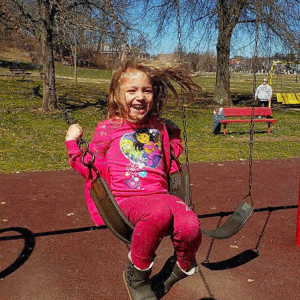 Gemma is registered to the contest to win money with this photo: child, fun, happy, joy, outdoor_play_equipment, person, pink, plant, play, playground, public_space, recreation, smile, swing, toddler, tree, vehicle