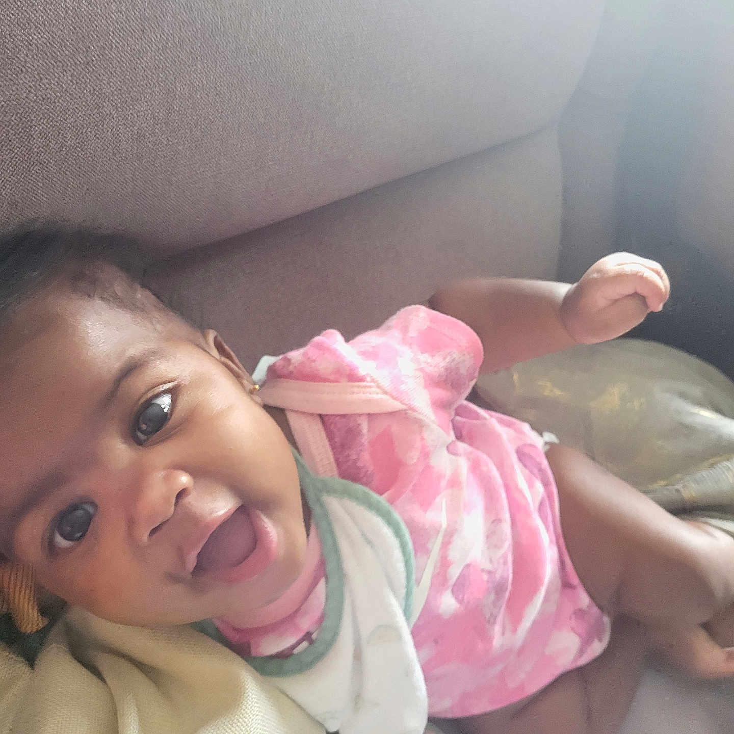 Luména participe au concours pour gagner de l'argent avec cette photo : baby, baby_bib, cheerful, child, couch, cute, face, happy, home, indoor, infant, laying_down, person, pink_clothing, portrait, relaxed, skin, small_hand, smiling, soft_lighting