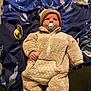 baby, infant, pacifier, onesie, knit_hat, blanket, batman_logo, blue_blanket, soft_clothing, cute, child, indoor, lying_down, face, headwear, comfort, warm_clothing, expression, foot, person