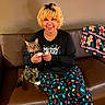 person, cat, tabby_cat, pet, indoors, living_room, couch, leather_sofa, holiday, christmas, festive, pajamas, light_bulbs, gingerbread, blanket, smiling, portrait, sitting, companion, cozy