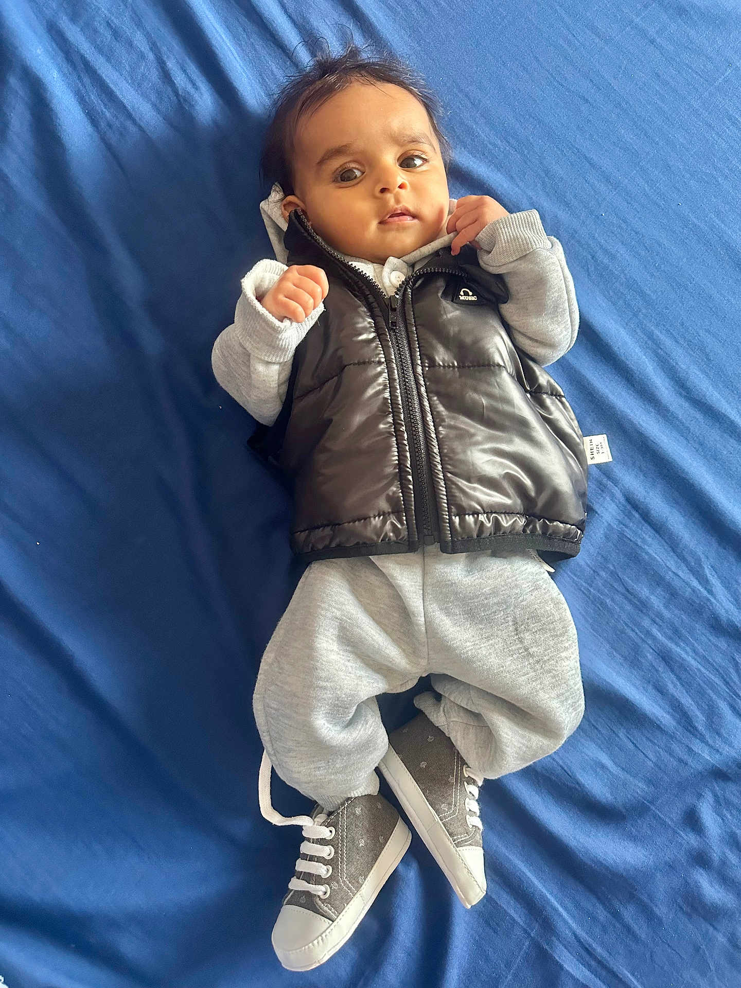 Dilawar joined the competition — help win amazing prizes! baby, infant, child, blue_bedspread, vest, sweatpants, sneakers, footwear, clothing, lying_down, indoor, portrait, cute, young_child, face, hands, expression, casual_wear, person, cozy