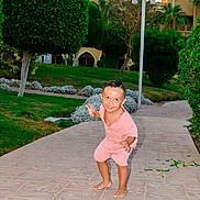 Yanis a rejoint le concours — aidez-le/la à gagner de superbes lots ! toddler, child, outdoor, pathway, greenery, bushes, tree, grass, building, playful, smiling, barefoot, pink_clothing, daylight, lamp_post, nature, garden, happy, cute, portrait
