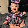 baby, child, smiling, headband, blue_eyes, colorful_clothing, patterned_outfit, indoor, bed, blanket, happy, person, cute, sitting, infant, portrait, clothing, headwear, cheerful, young