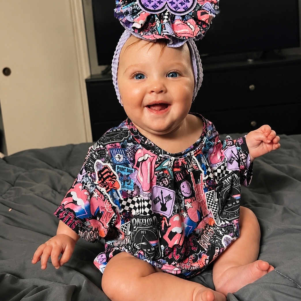 Saylor joined the competition — help win amazing prizes! baby, child, smiling, headband, blue_eyes, colorful_clothing, patterned_outfit, indoor, bed, blanket, happy, person, cute, sitting, infant, portrait, clothing, headwear, cheerful, young