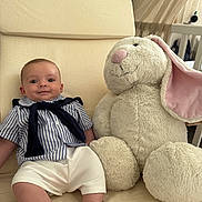 Owen a rejoint le concours — aidez-le/la à gagner de superbes lots ! baby, child, stuffed_animal, bunny, plush_toy, striped_shirt, white_shorts, indoor, chair, cushion, smiling, cute, soft_toy, comfort, home, portrait, feet, sitting, fabric, relaxing