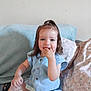 blue_outfit, casual_clothing, child, couch, fingers_in_mouth, girl, hair_tie, happy, home, indoor, light_skin, person, pillows, plastic_container, playful, relaxed, sitting, smiling, toddler, toys