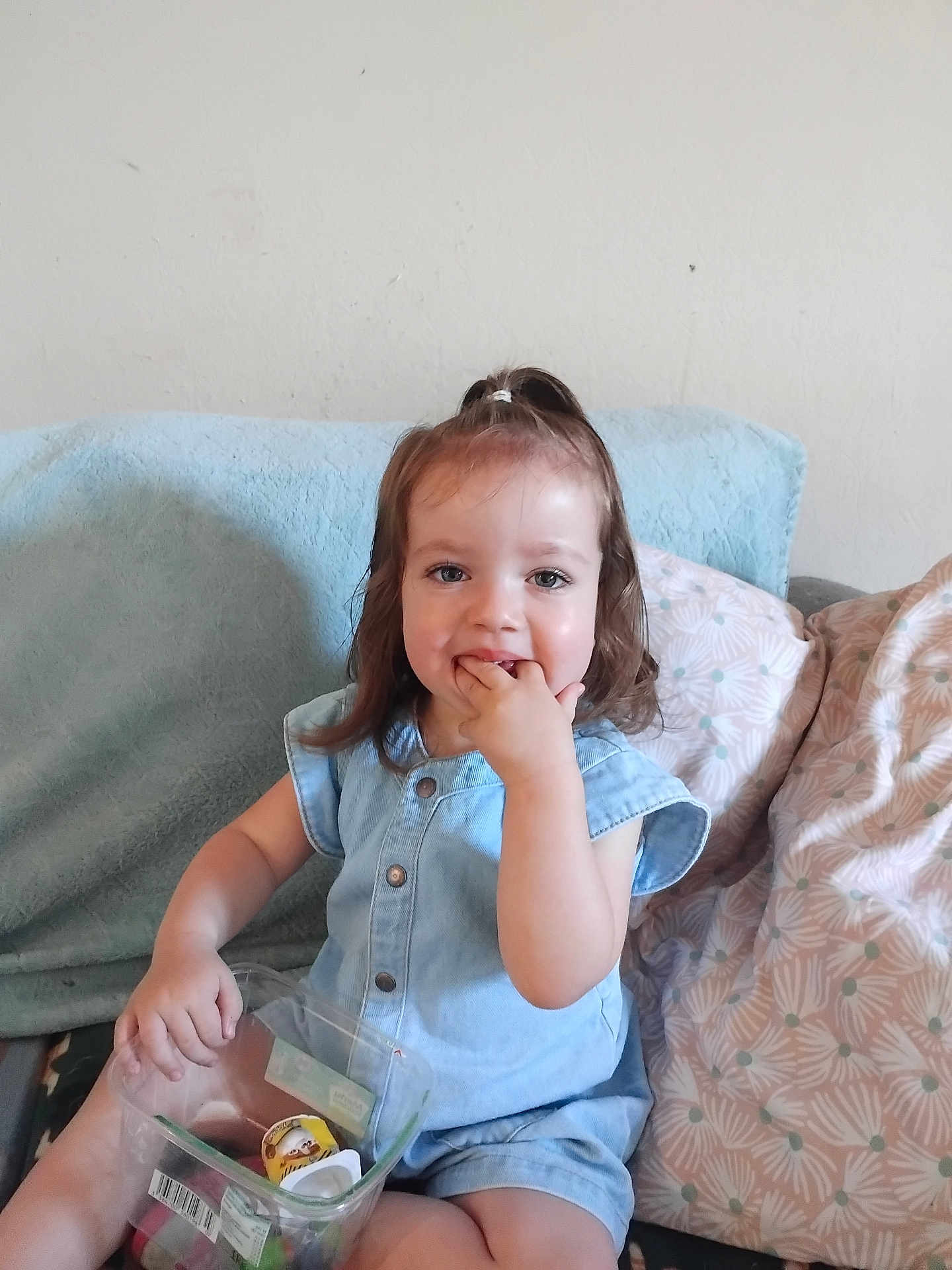 Alma a rejoint le concours — aidez-le/la à gagner de superbes lots ! blue_outfit, casual_clothing, child, couch, fingers_in_mouth, girl, hair_tie, happy, home, indoor, light_skin, person, pillows, plastic_container, playful, relaxed, sitting, smiling, toddler, toys