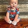 baby, child, infant, sitting, colorful_clothing, white_socks, wooden_surface, pacifier, background_wood, cute, curious, indoor, portrait, face, hands, feet, light_skin, short_hair, blue_eyes, patterned_outfit