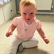 Harley joined the competition — help win amazing prizes! baby, child, red_hair, pink_bib, light_pants, sitting, carpet, indoor, smiling, face, blue_eyes, cute, playful, person, young_child, floor, toy, clothing, room, home