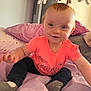Harley is registered to the contest to win money with this photo: baby, child, smiling, sitting, bed, pillow, blanket, plush_toys, mobile, pink_shirt, neon, indoor, cozy, cute, happy, face, person, young_child, soft_lighting, casual_clothing