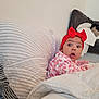 Athéna participe au concours pour gagner de l'argent avec cette photo : baby, red_bow, headband, surprised_expression, pillow, blanket, bed, indoors, child, clothing, patterned_clothes, person, face, cozy, soft_furnishing, cute, infant, home, sleepwear, resting