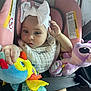 baby, child, car_seat, pink, headband, bow, plush_toy, colorful, infant, seatbelt, cute, soft_toys, indoors, person, skin, hand, clothing, portrait, young, seat